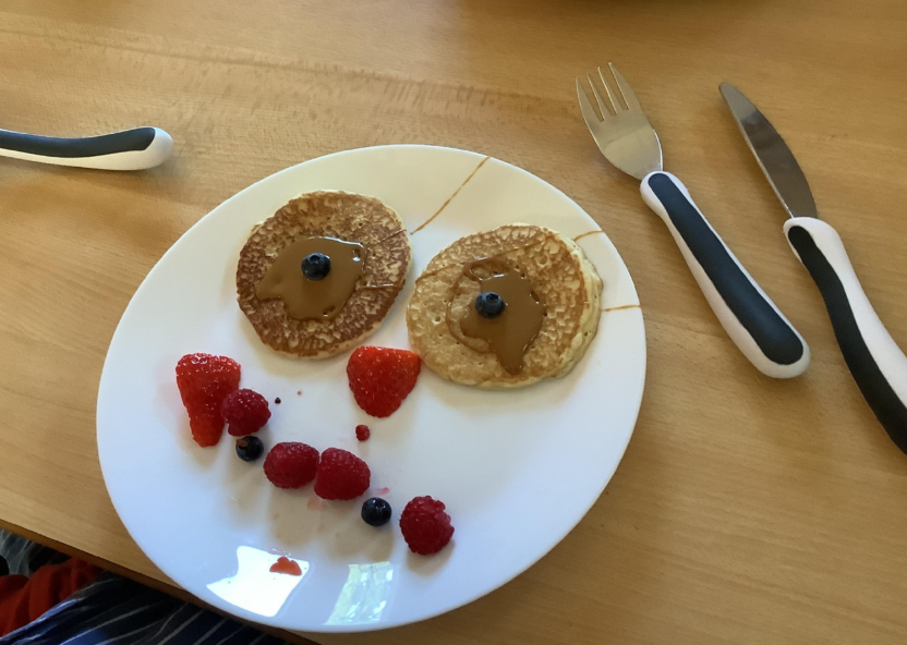 A plate of food with pancakes and berries made to look like a smiley face